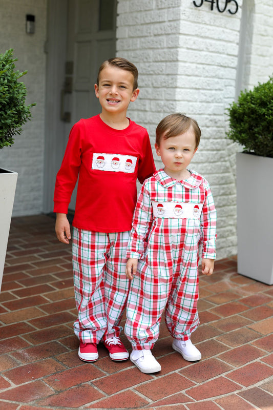 Two children wearing matching red and plaid pajamas standing on a brick patio.