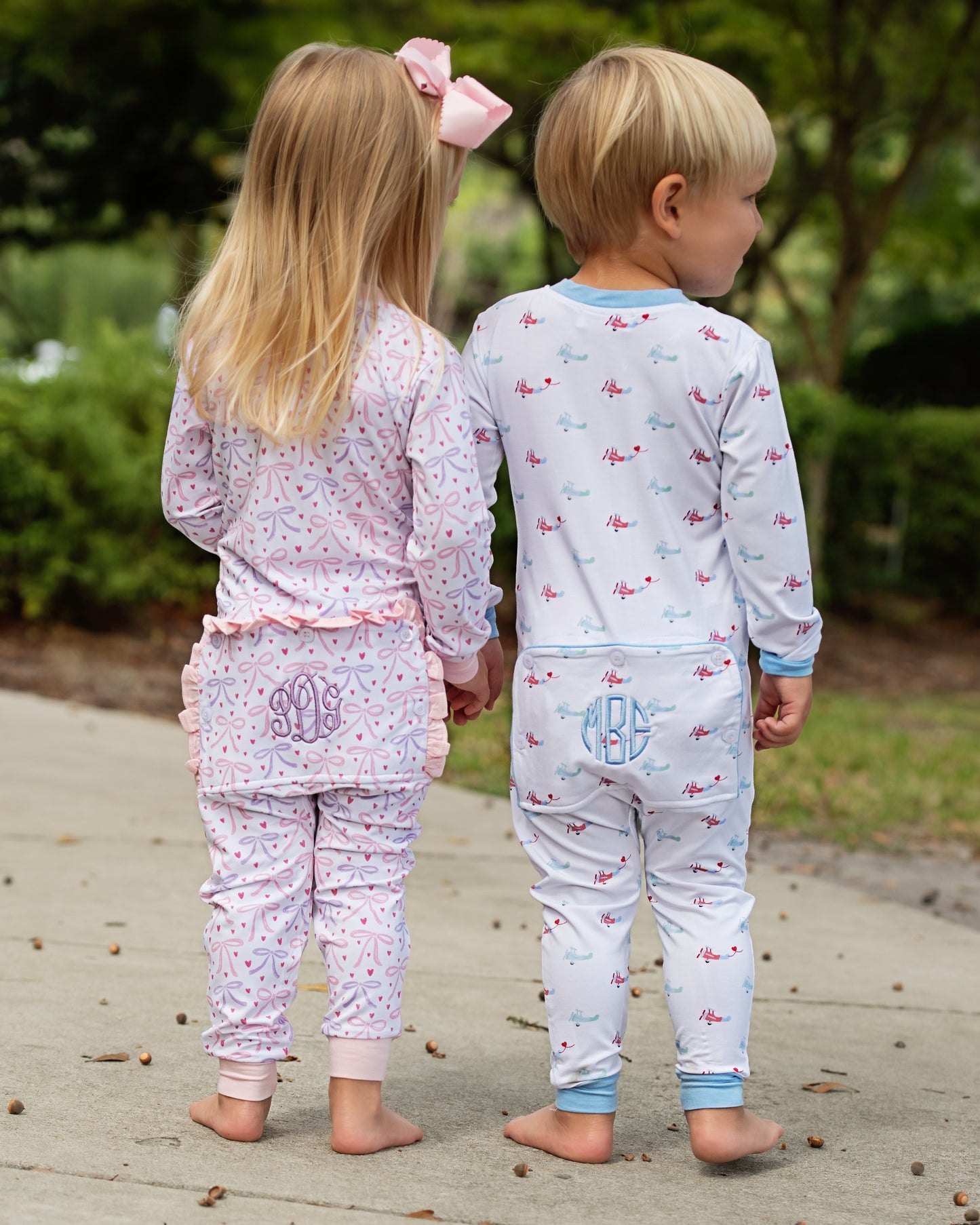 Two children wearing matching zipper pajamas with a garden background