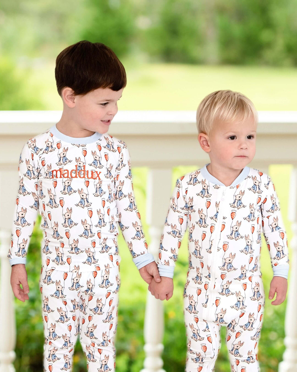 Two children wearing pajamas with a pattern of animals and text, standing on a wooden deck.