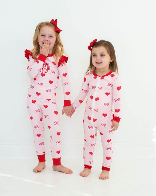 Two children wearing pink pajamas with red hearts and bows on a white background
