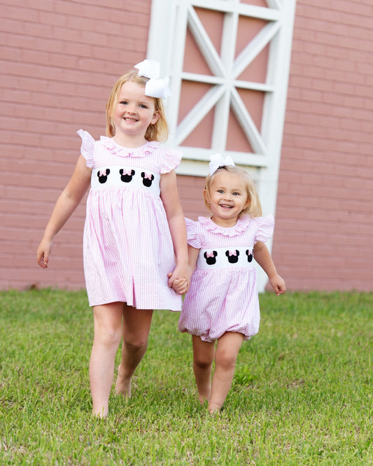 Two girls holding hands wearing smocked mouse ears seersucker dress and bubble