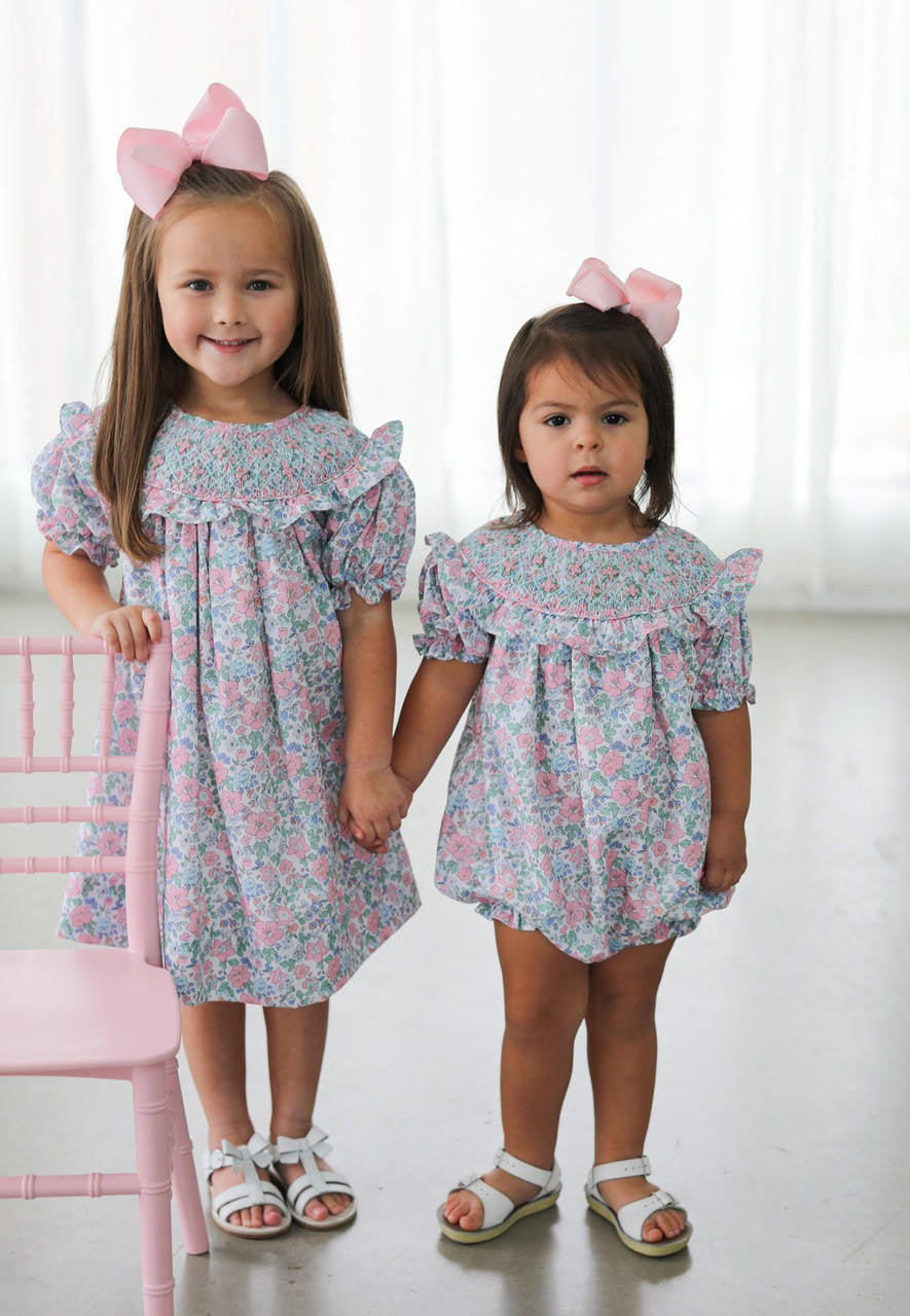 Two little girls wearing a matching dress and bubble holding hands
