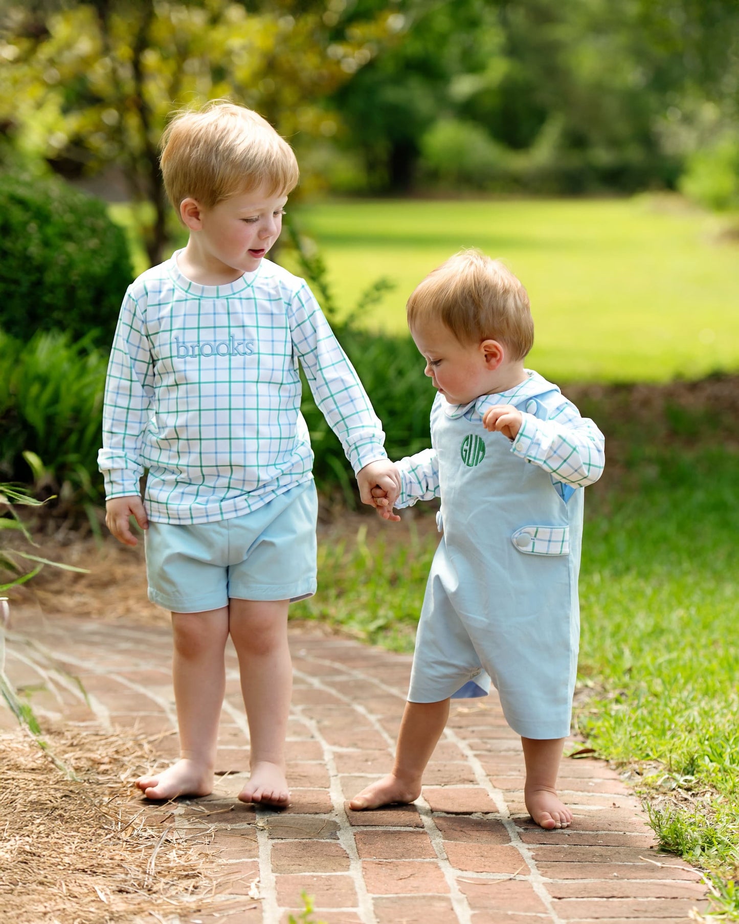Two young boys holding hands on a brick path with greenery in the background