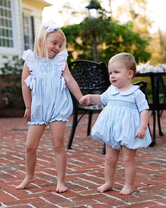Two young children in matching blue checkered outfits standing on a brick patio.