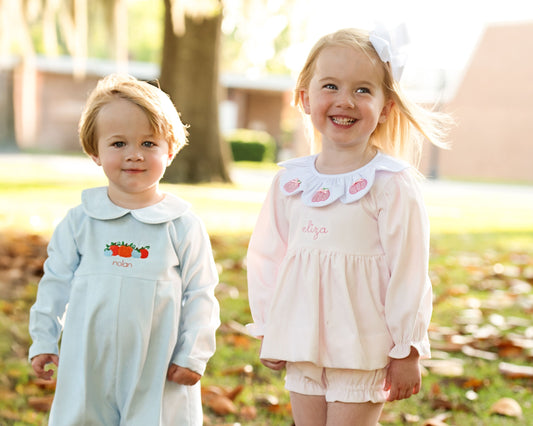 Two young children in matching outfits standing outdoors with trees and grass in the background.