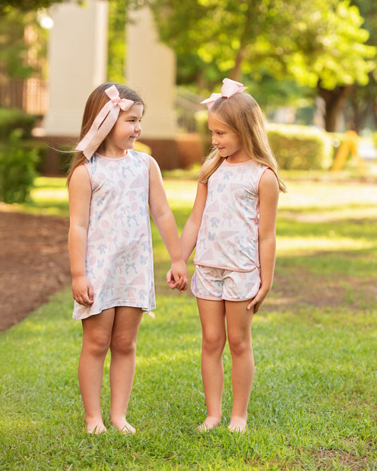Two young girls holding hands in matching outfits on a grassy outdoor setting.