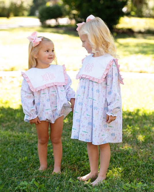 Two young girls in matching birthday bubble and dress standing on grass outdoors.
