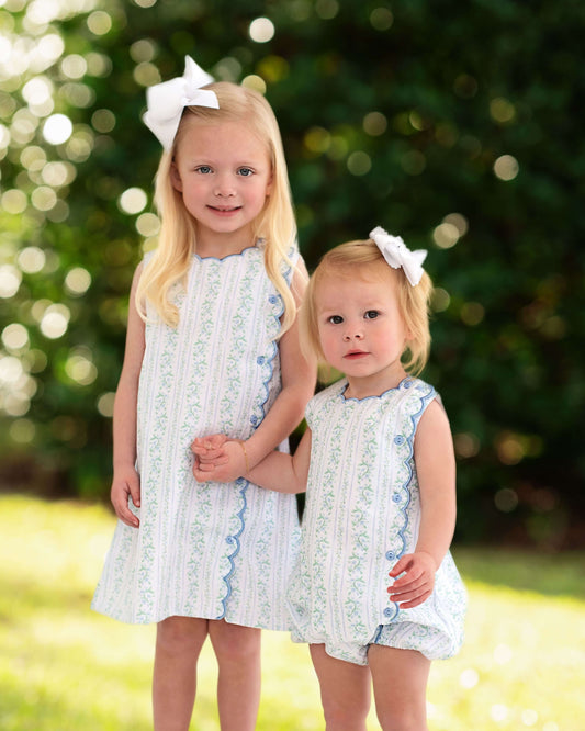 Two young girls in matching dress and bubble standing outdoors with a blurred green background