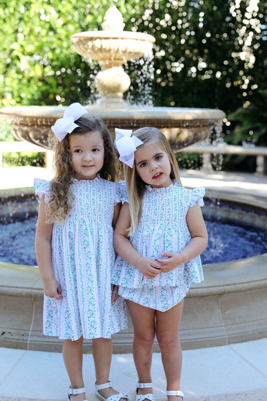 Two young girls in matching dresses standing in front of a fountain.