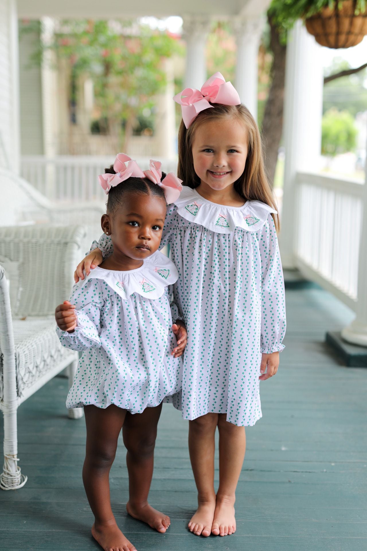 Two young girls in matching dresses with bows standing on a porch.