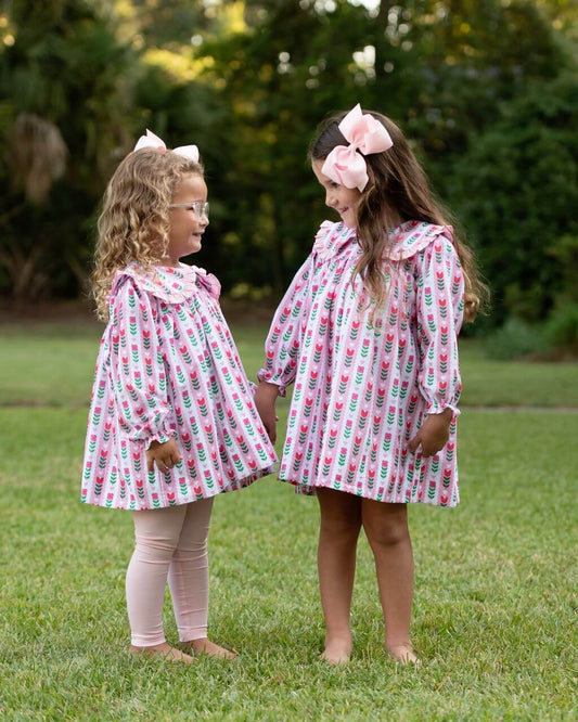 Two young girls in matching dresses with floral patterns standing on grass.