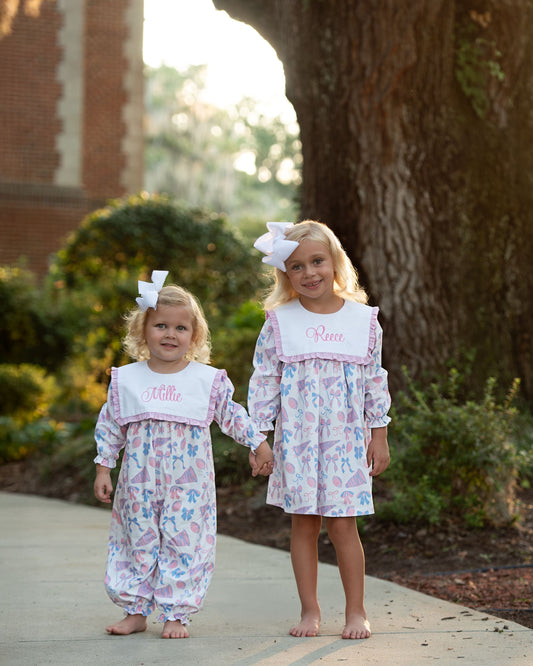 Two young girls in matching floral outfits standing outdoors near a large tree.