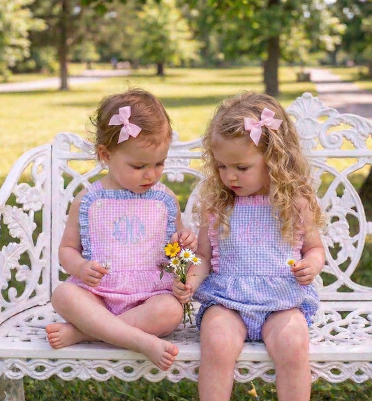 Two young girls in matching outfits sitting on a white bench in a park.