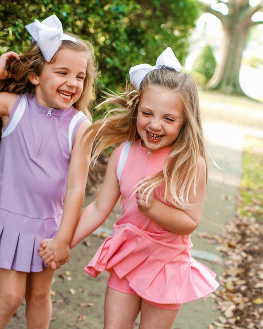 Two young girls in matching outfits with bows, laughing outdoors.