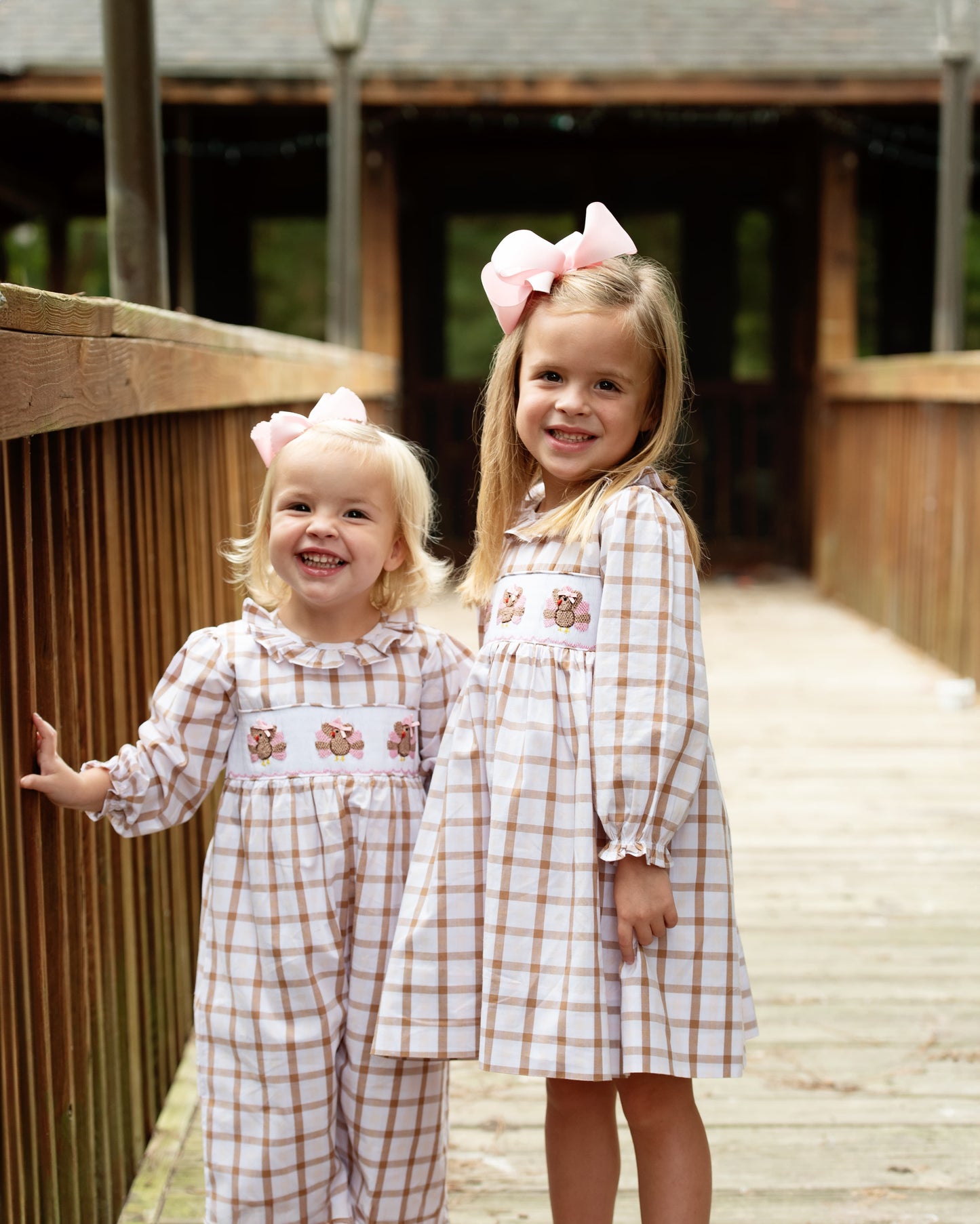 Two young girls in matching outfits with embroidered turkeys and bows standing on a wooden pathway