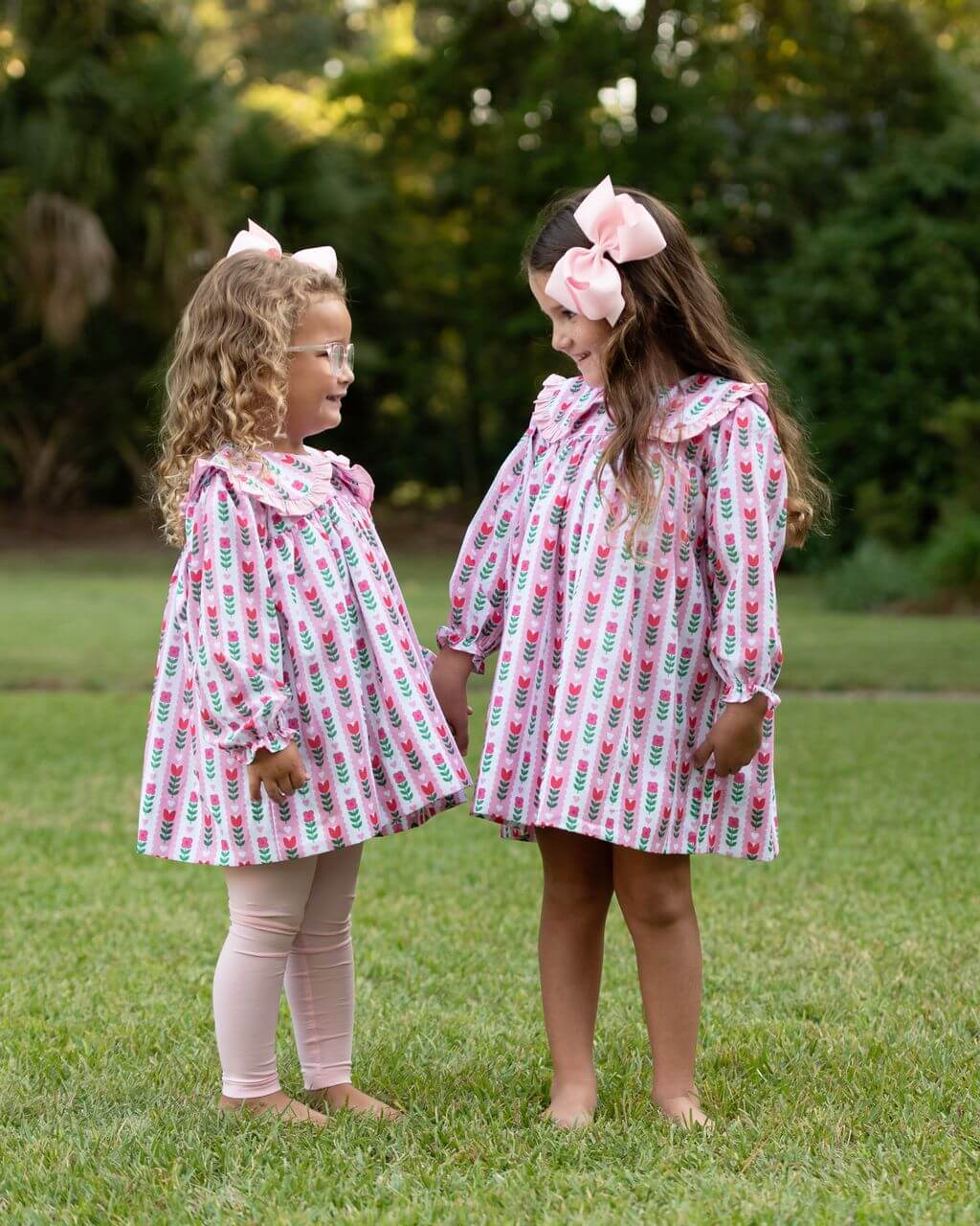 Two young girls in matching outfits with floral patterns standing on grass.