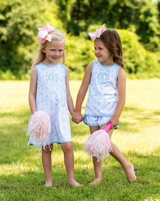 Two young girls in matching outfits with pink pom-poms standing on grass.