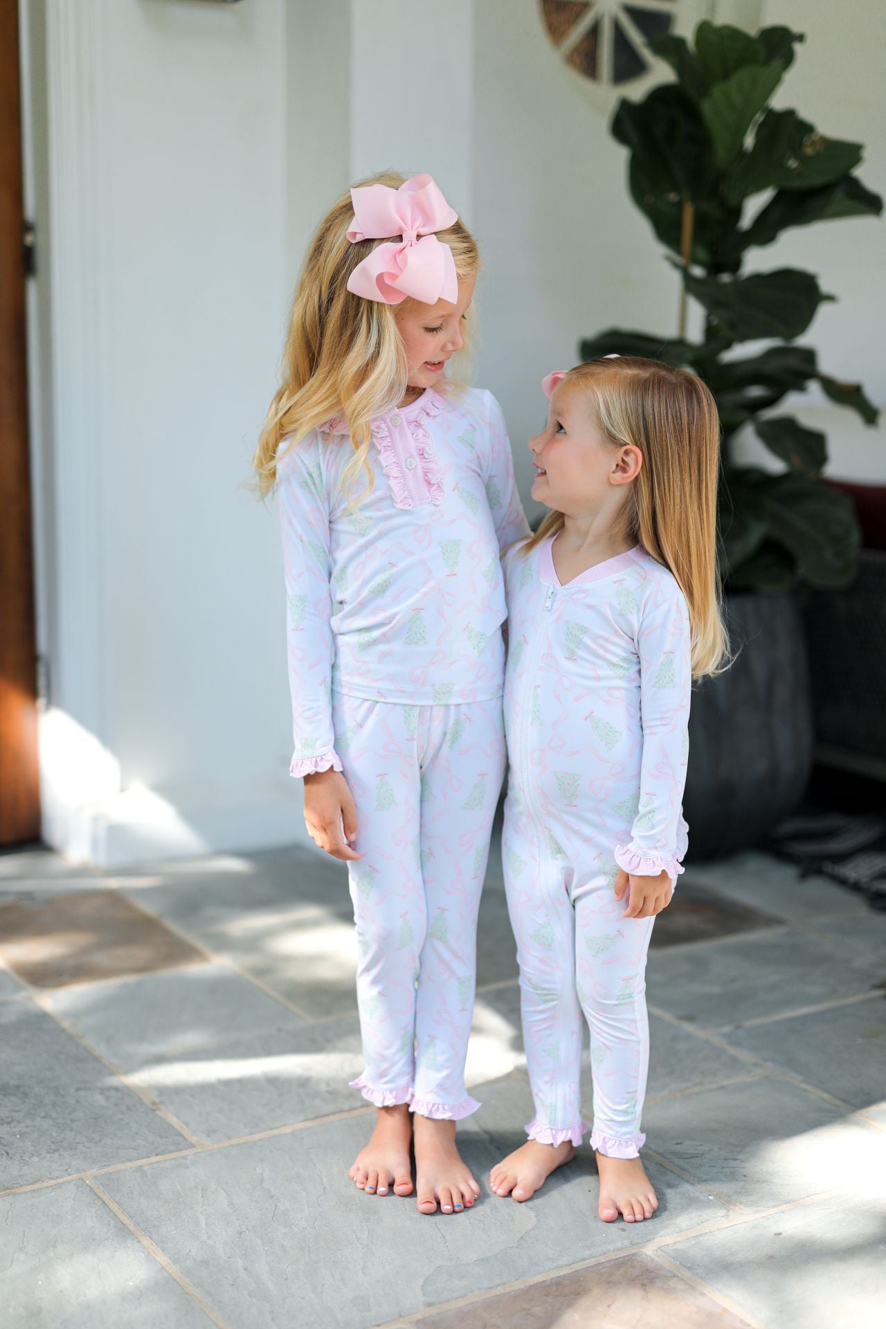 Two young girls in matching pajamas standing on a stone patio.