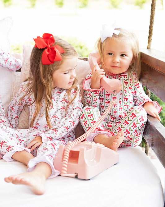 Two young girls in matching pajamas with a red and white pattern, sitting on a couch.