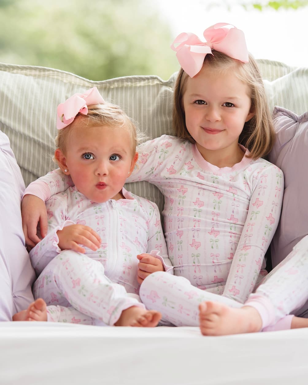 Two young girls in matching pajamas with pink bows sitting on a couch.