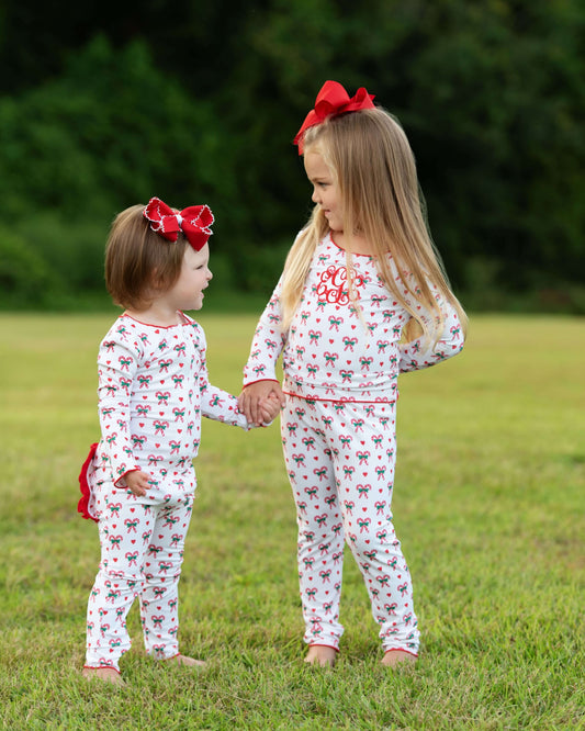 Two young girls in matching pajamas with red bows standing in a grassy field.