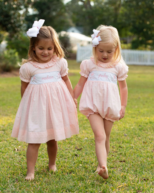 Two young girls in matching pink dresses walking on grass.