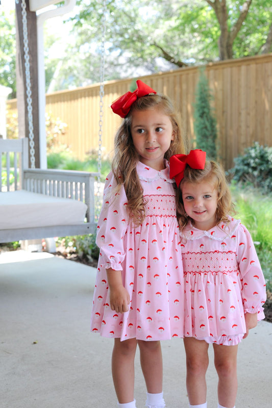 Two young girls in matching pink dresses with red bows outdoors.