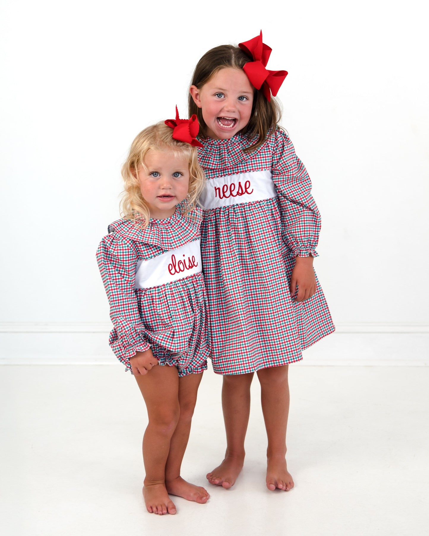 Two young girls in matching red, white, and green gingham dresses with white name patches.