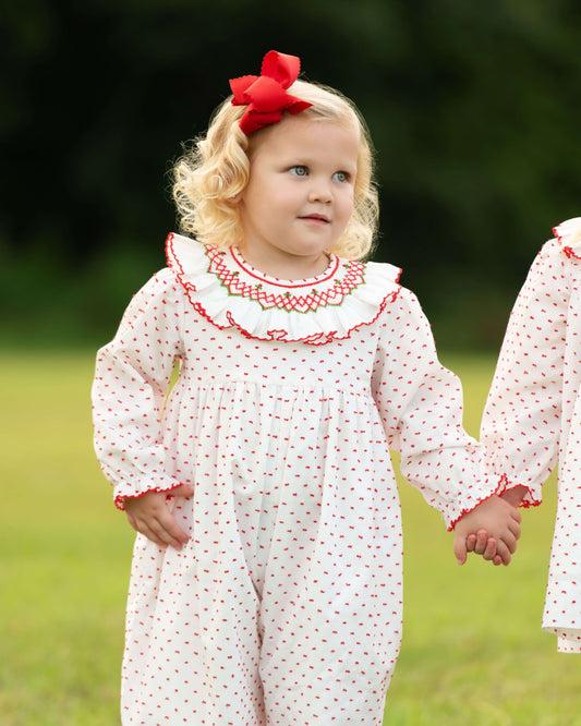 Two young girls in matching white dresses with red trim standing in a grassy field.