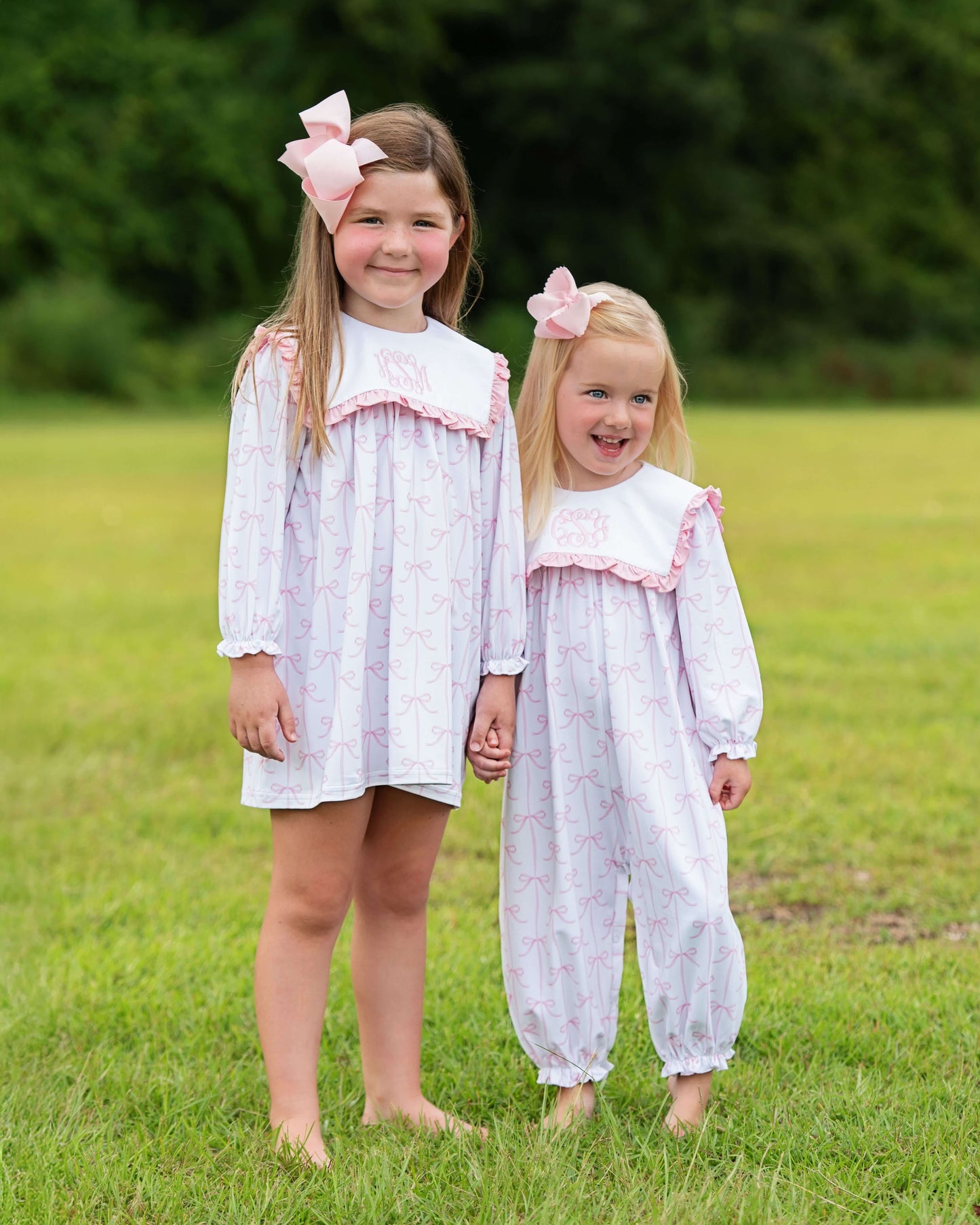 Two young girls in matching white outfits with pink accents standing on grass.