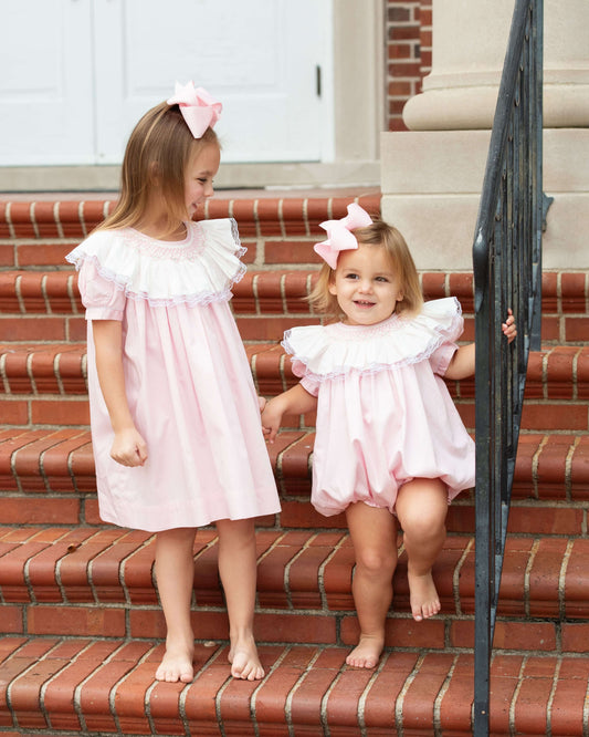 Two young girls in pink dresses standing on a set of red brick stairs.
