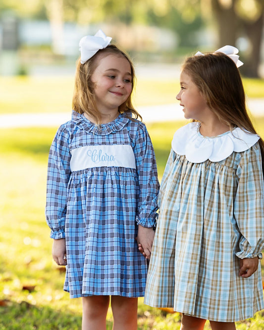 Two young girls in plaid dresses standing outdoors with a blurred background