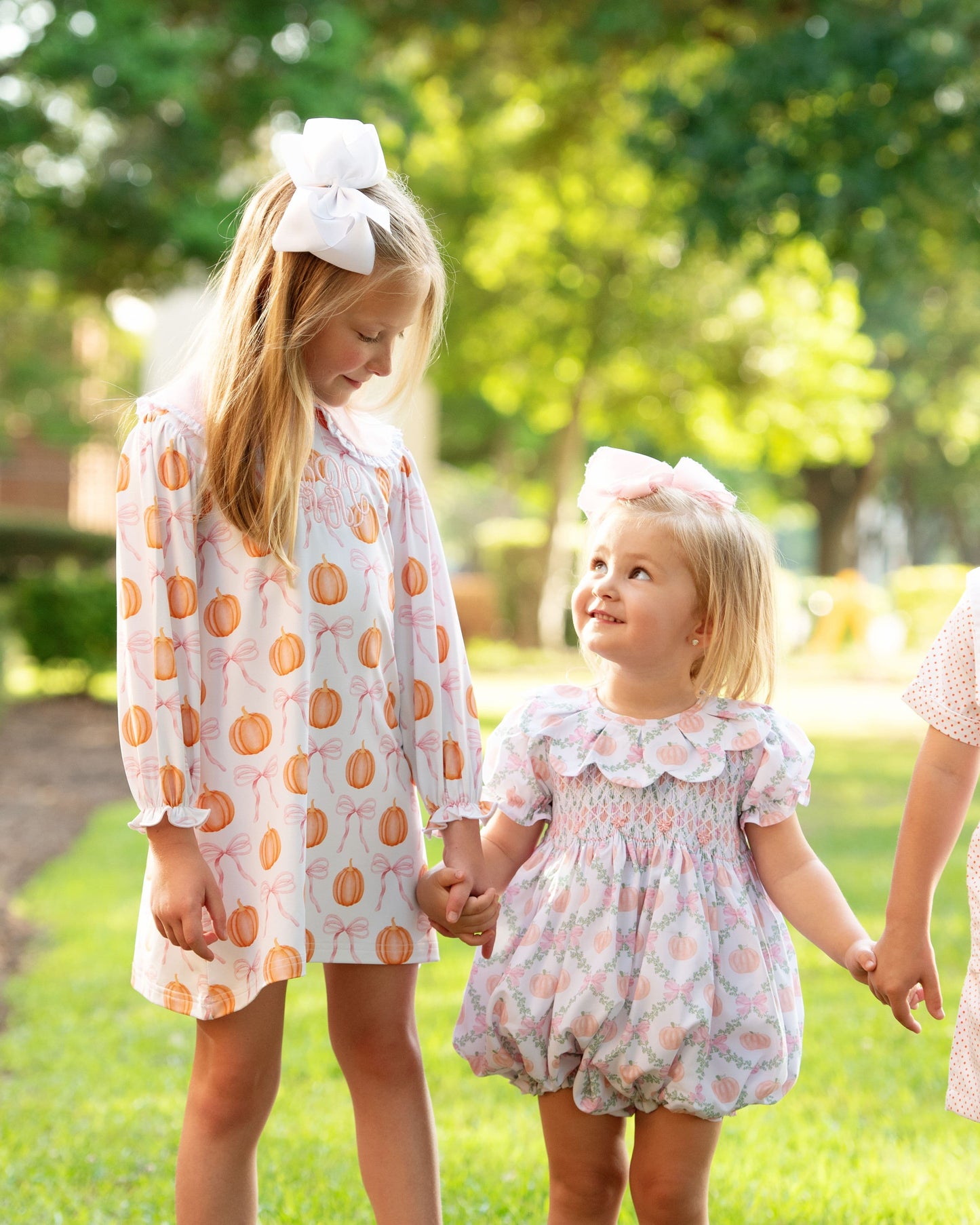 Two young girls in pumpkin outfits standing outdoors with greenery in the background