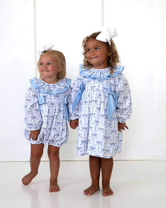 Two young girls wearing matching blue and white dresses with ruffled collars on a white background.