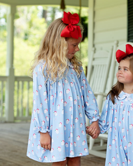 Two young girls wearing matching blue dresses with red bows on a porch.