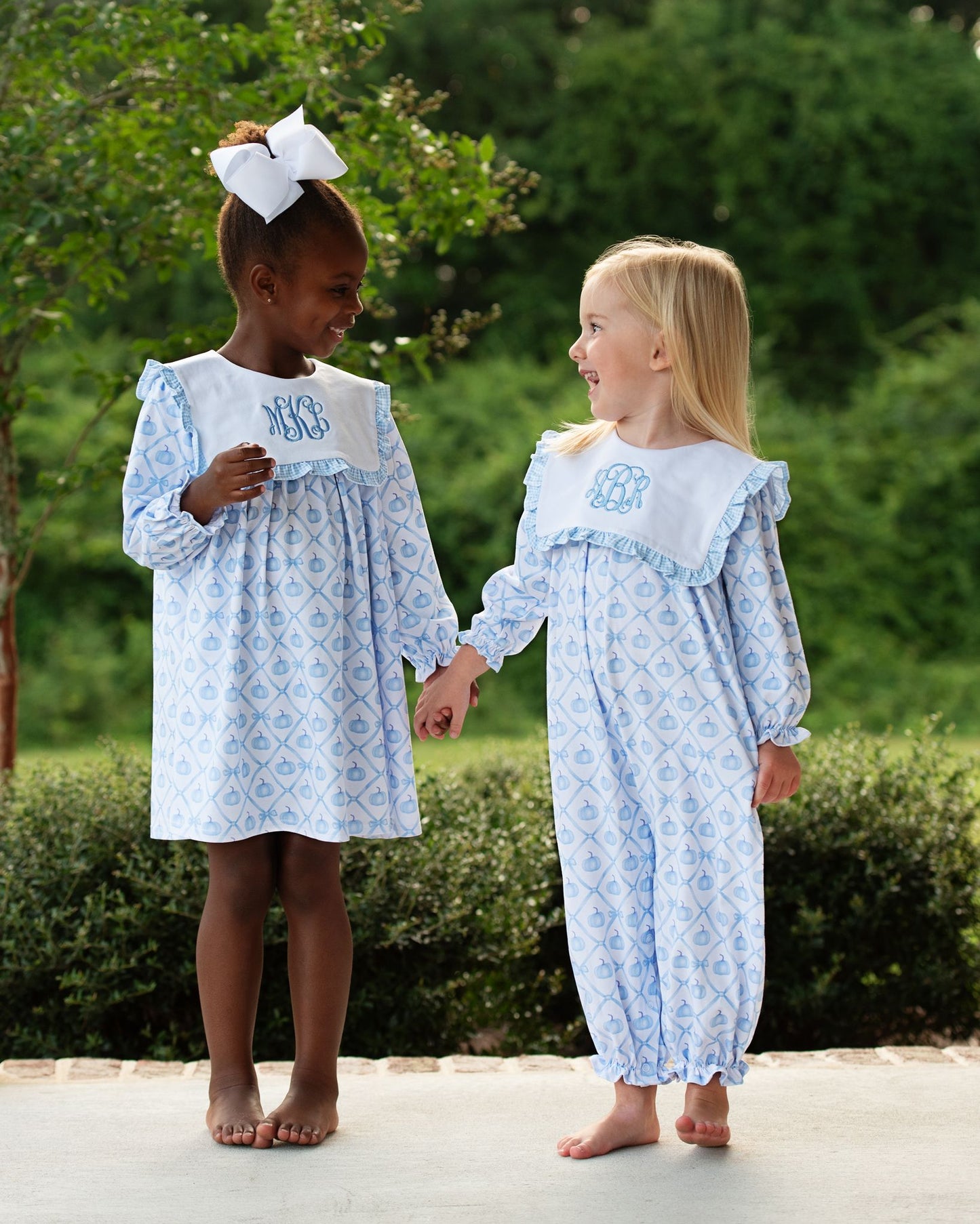 Two young girls wearing matching blue dresses with white patterns, standing outdoors.