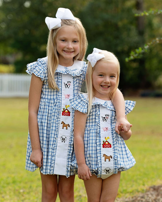 Two young girls wearing matching dresses with embroidered designs outdoors.