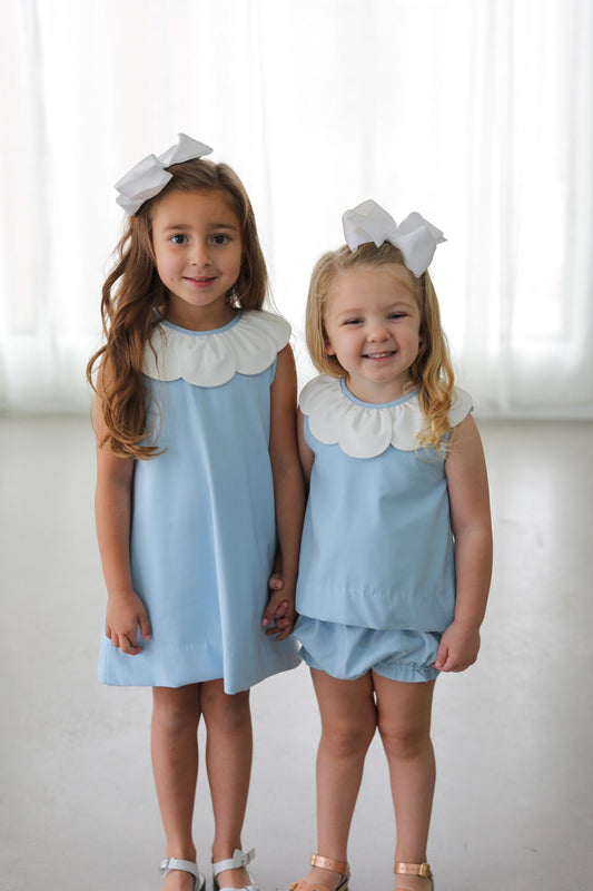 Two young girls wearing matching light blue dresses with white collars against a white background.