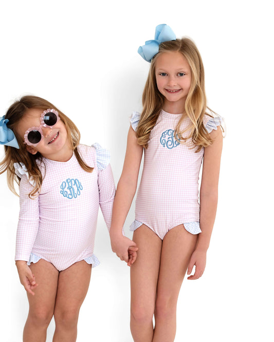Two young girls wearing matching pink checkered swimsuits with sunglasses and bows on a white background