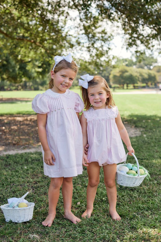Two young girls wearing matching pink outfits, standing outside with Easter baskets