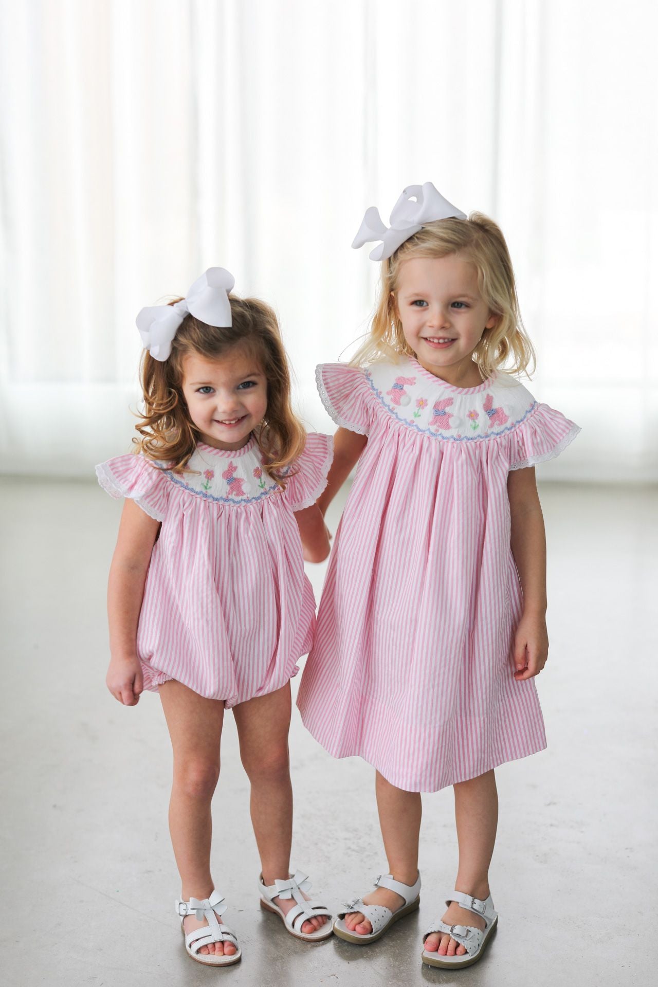Two young girls wearing matching pink outfits with white bows on a white background