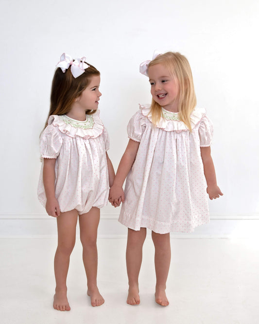 Two young girls wearing matching white dresses with lace details on a white background