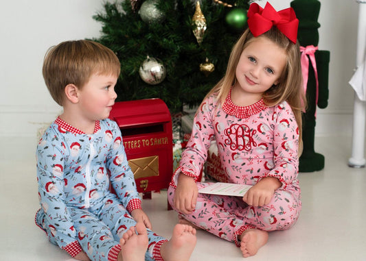 Two children wearing matching Santa pajamas, sitting on the floor in front of a Christmas tree