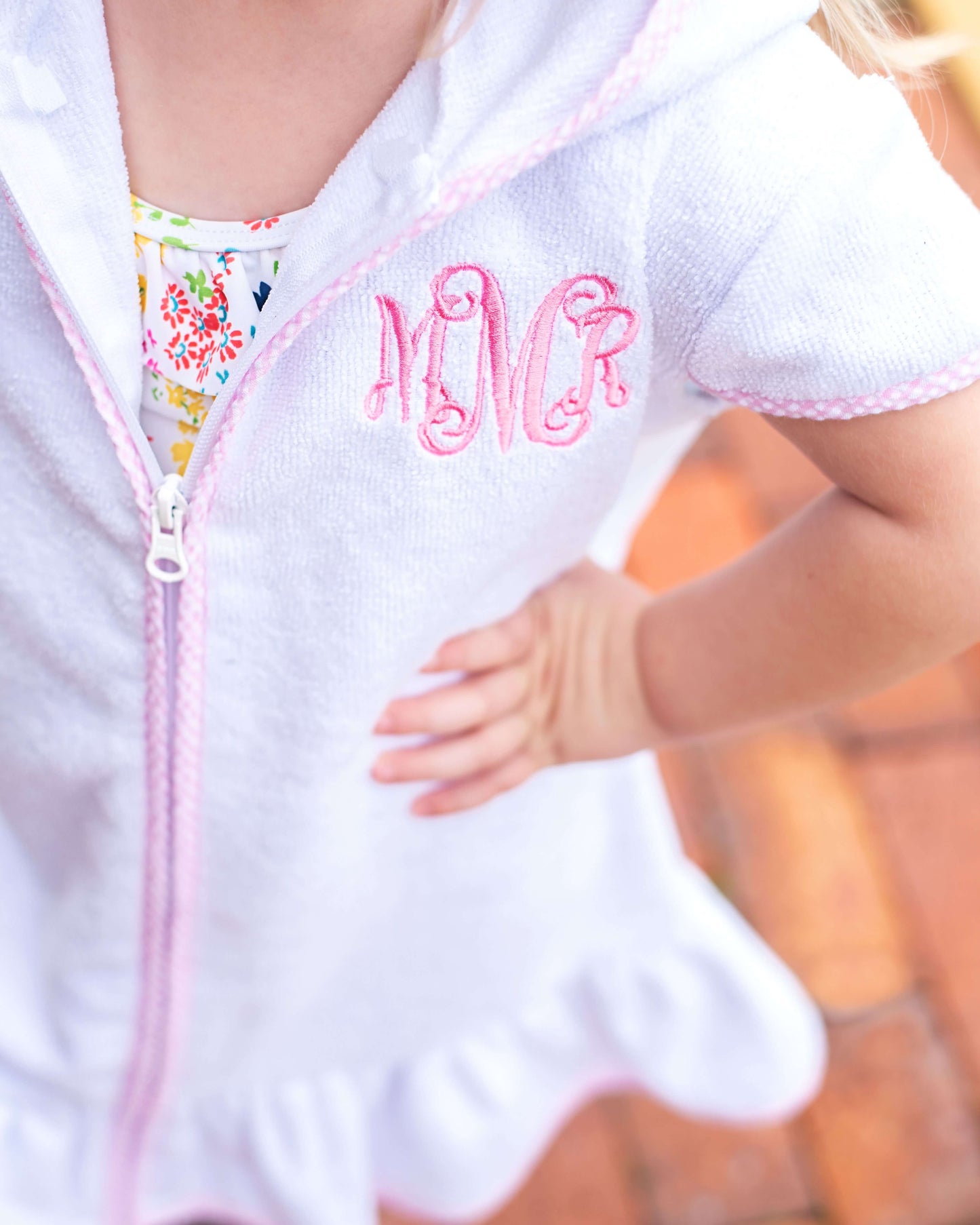 White baby romper with pink lettering worn by a child, blurred background
