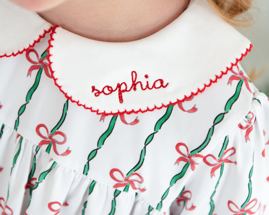 White dress with red and green ribbon pattern and 'sophia' embroidery