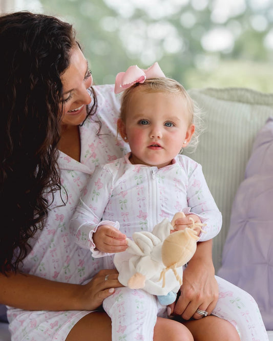 Woman and baby in matching pajamas holding a plush toy outdoors.