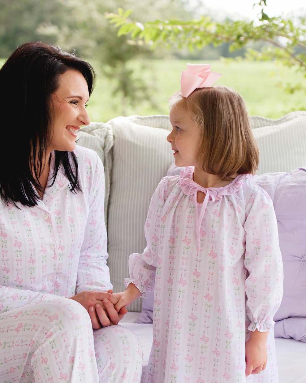 Woman and child in matching pajamas sitting on a couch outdoors.