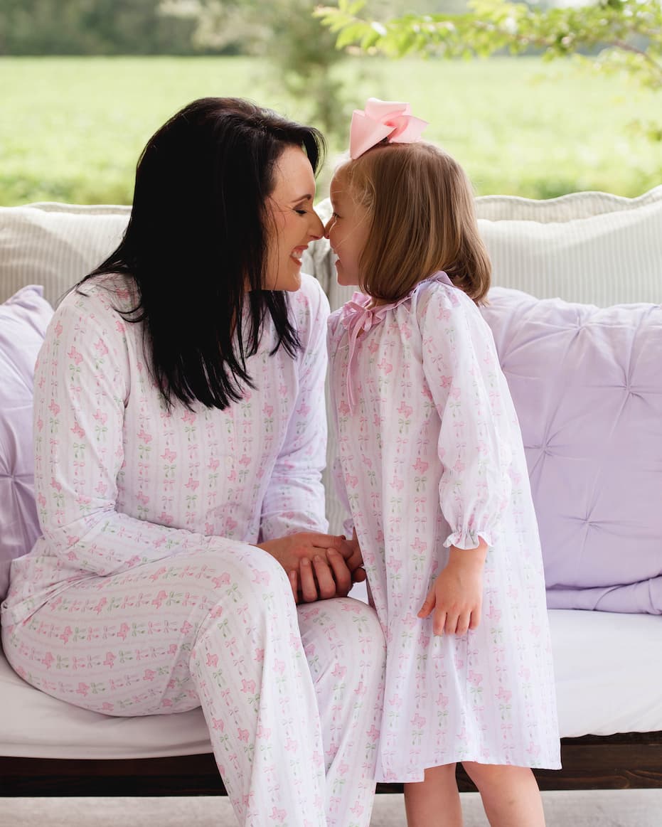 Woman and young girl in matching pajamas sitting on a couch outdoors.