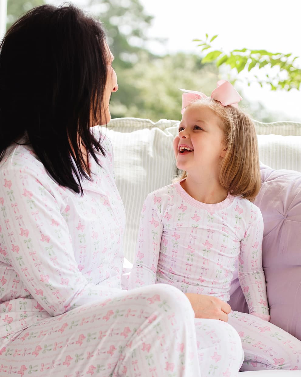 Woman and young girl sitting on a couch wearing matching pajamas with a floral pattern.