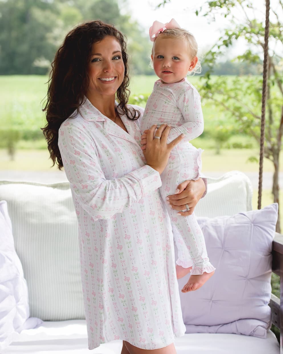 Woman holding a baby in a matching white outfit outdoors